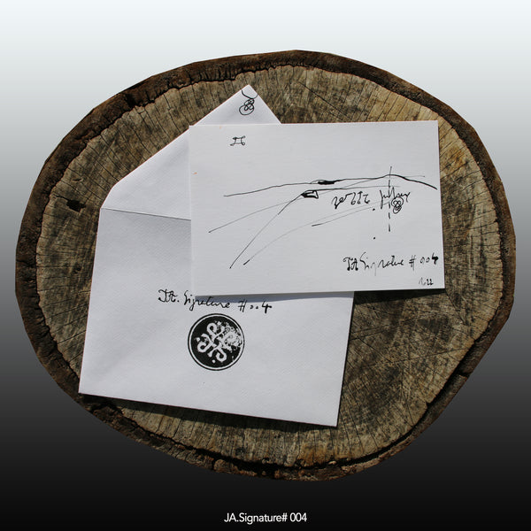 JA.SIGNATURE#004 NFT created from the physical collection JA.Signature by James Arax. On the picture : On a log, in the foreground the JA.Signature paper card and below the envelope with the number of the NFT t and james sign (LogoType).